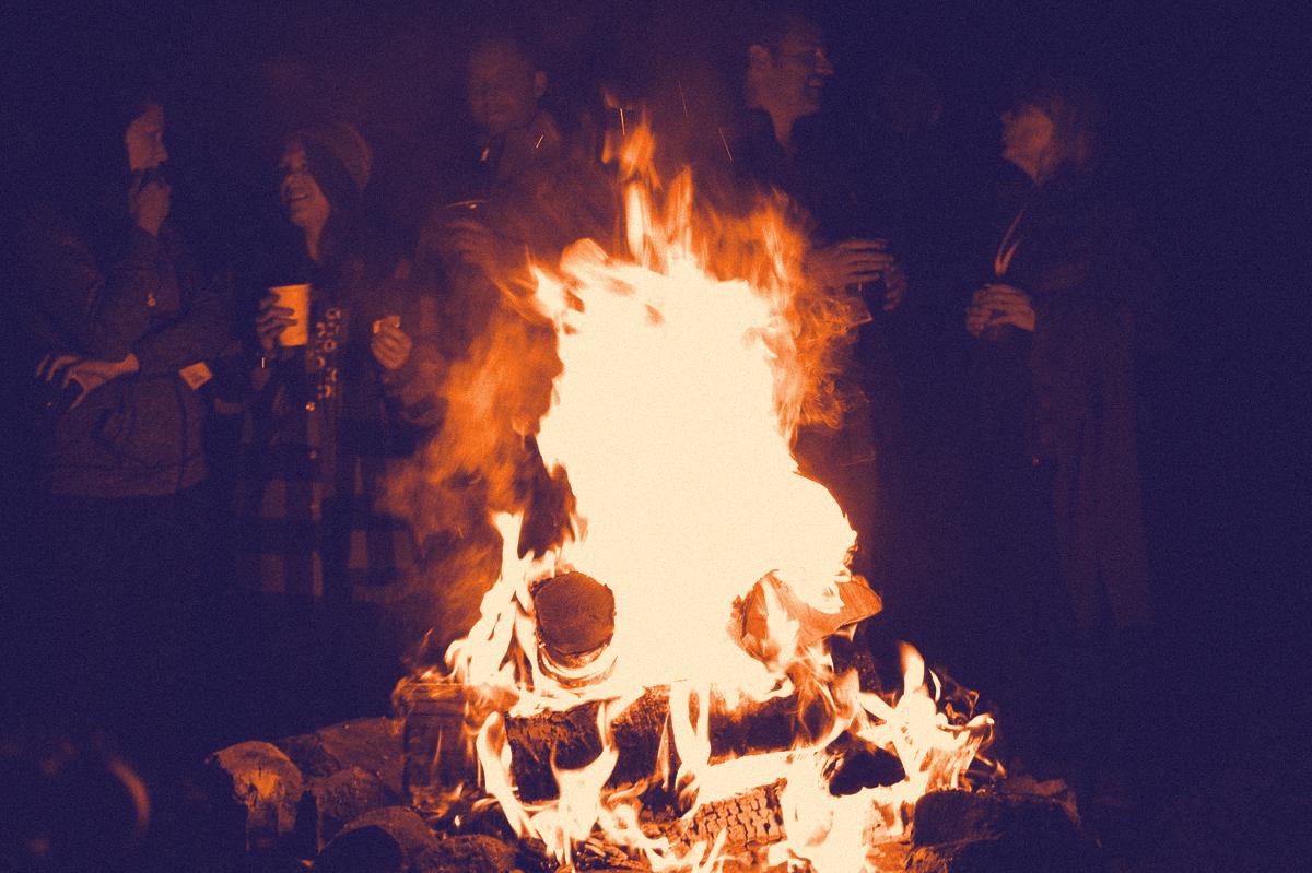 Campers laughing around a roaring campfire at night