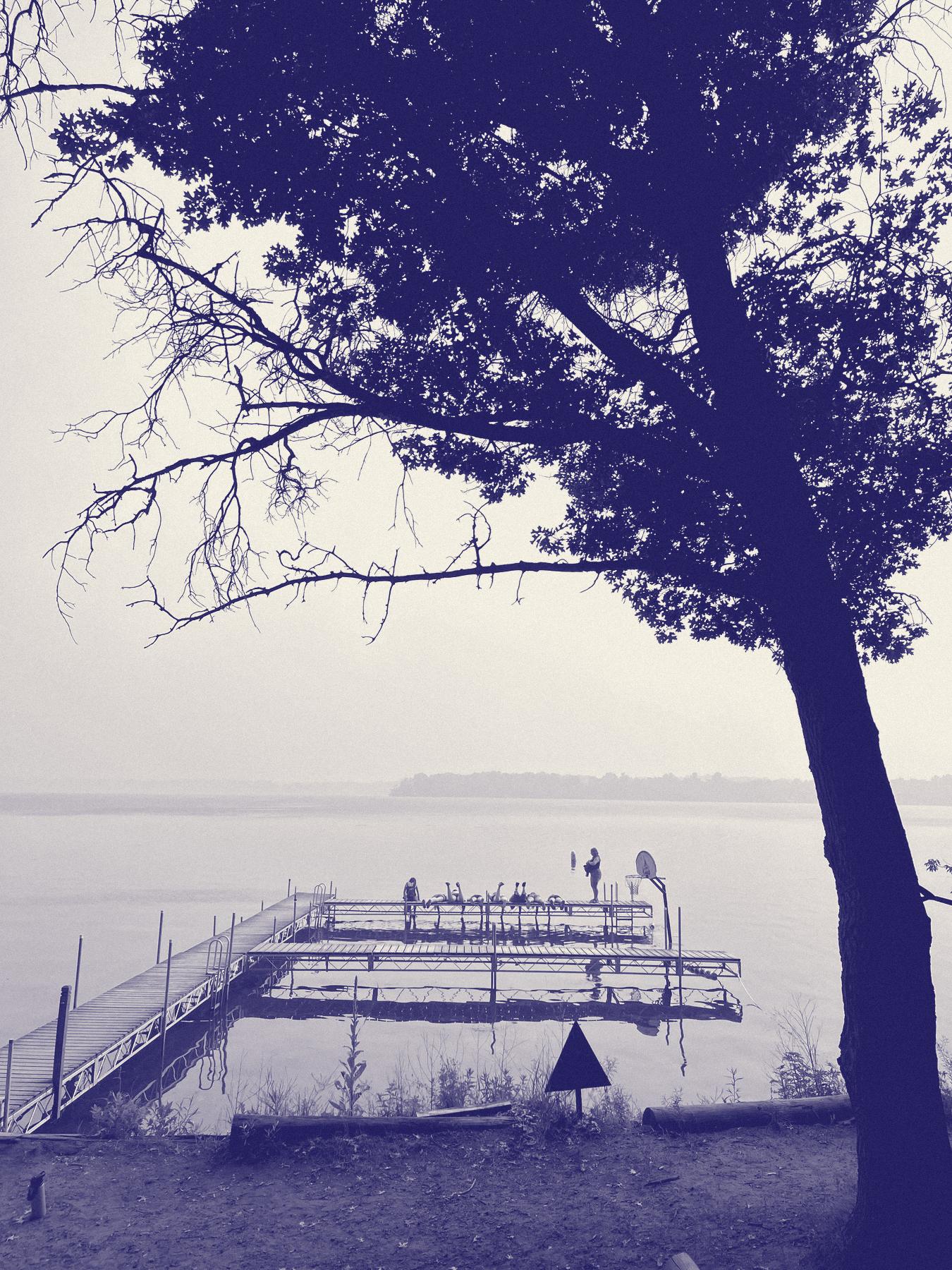 Campers stretched out on the dock at Camp Icaghowan, under a big oak on a hazy morning